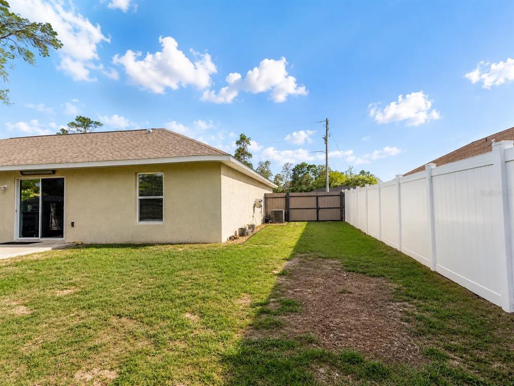 A backyard view shows a tan house exterior, a white vinyl fence, and a gate — 17023 SW 41ST AVENUE, OCALA, FL