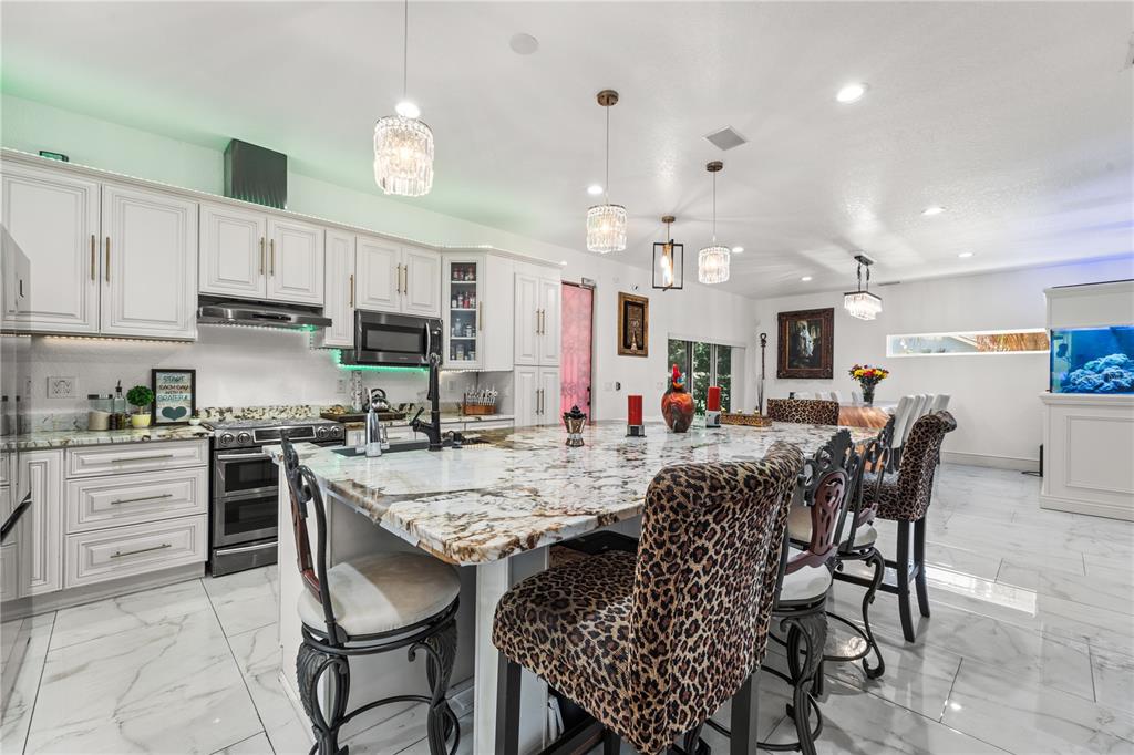 A kitchen features white cabinetry, a large marble-topped island, and leopard-print bar stools — 2520 GOMAZ WAY S, ST PETERSBURG, FL