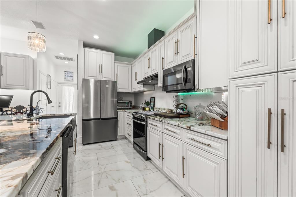 A kitchen features white cabinetry, marble-patterned countertops, stainless steel appliances, and light-colored tile flooring — 2520 GOMAZ WAY S, ST PETERSBURG, FL