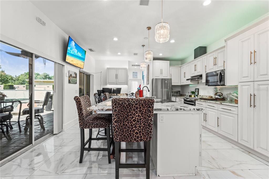 A modern kitchen features white cabinetry, a marble-topped island with leopard-print stools, and tile flooring — 2520 GOMAZ WAY S, ST PETERSBURG, FL