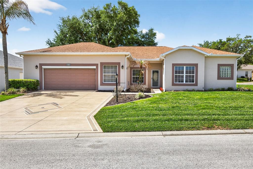 A single-story suburban house with a tan stucco exterior, brown roof, and two-car garage — 5036 SAWGRASS LAKE CIRCLE, LEESBURG, FL