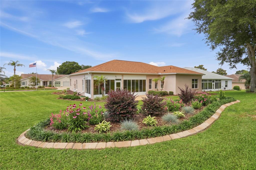 A single-story house with a tan exterior, a screened-in porch, and a landscaped garden bed — 5036 SAWGRASS LAKE CIRCLE, LEESBURG, FL