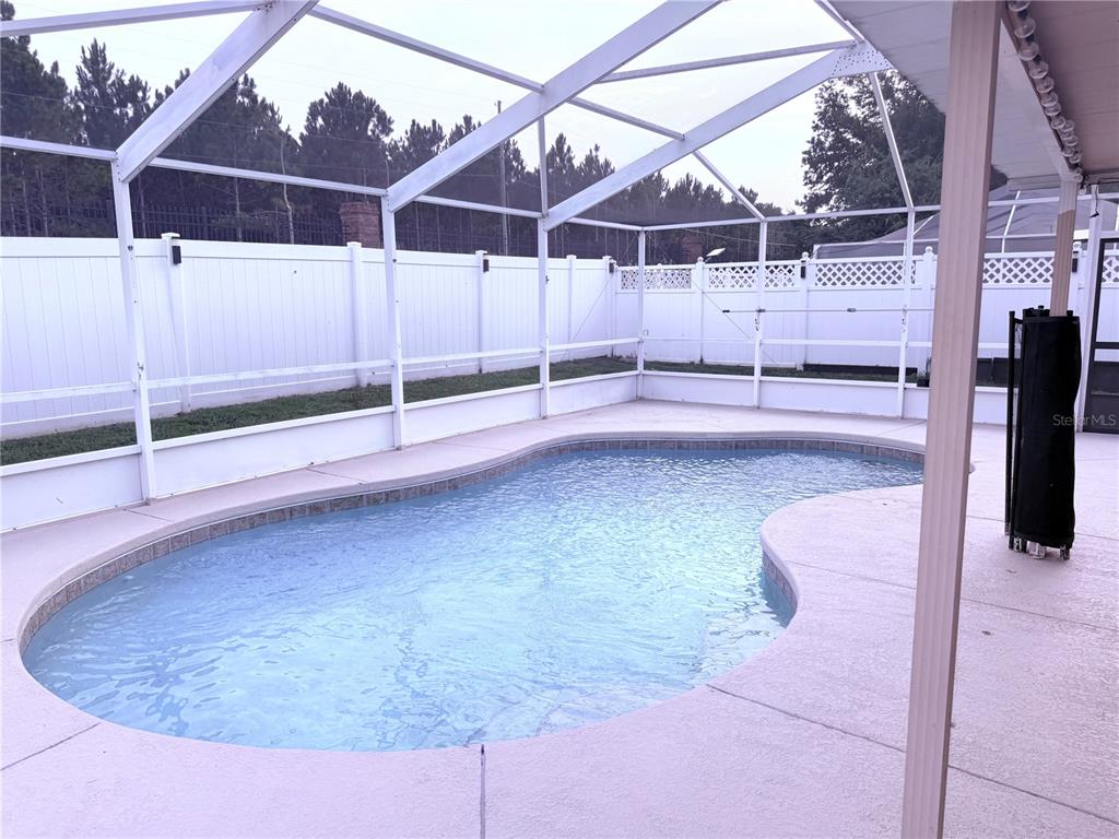 A swimming pool is enclosed by a white screen cage and a white privacy fence — 161 CHINA BERRY CIRCLE, DAVENPORT, FL