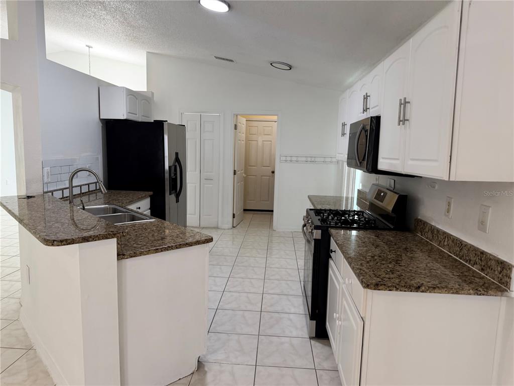 A kitchen features white cabinets, granite countertops, a stainless steel refrigerator, and tiled flooring — 161 CHINA BERRY CIRCLE, DAVENPORT, FL