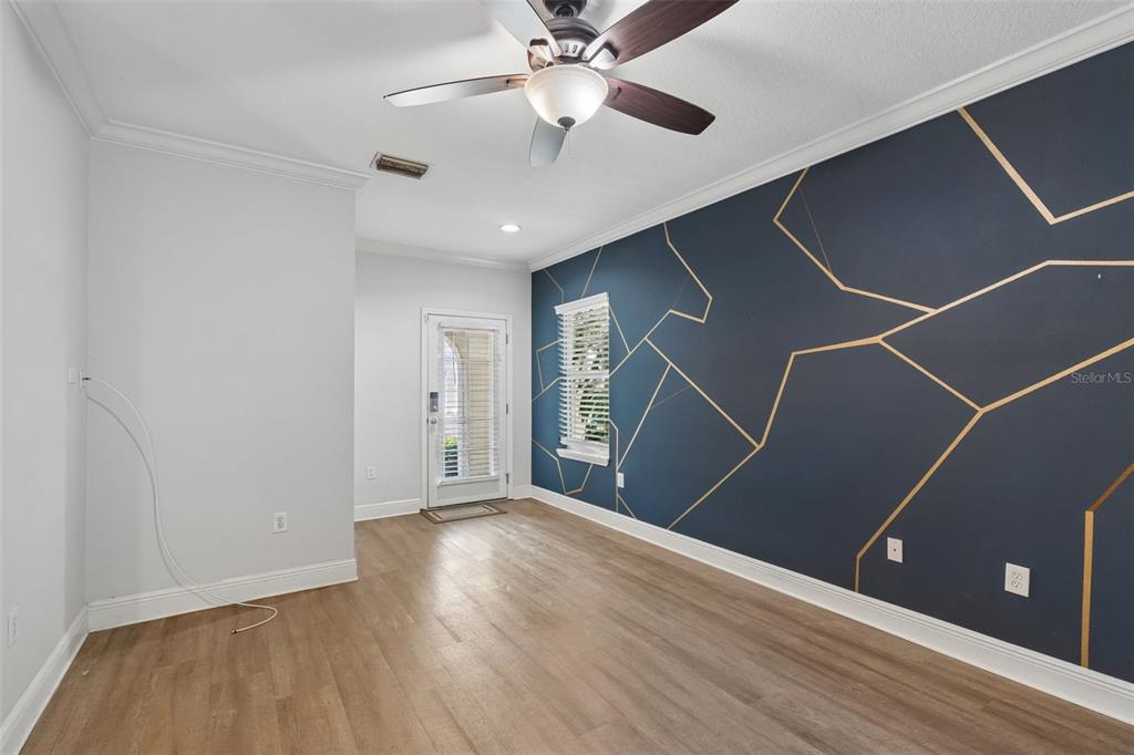 A room with wood-look flooring, a ceiling fan, and a dark accent wall with gold lines — 3125 SANTORINI COURT, TAMPA, FL