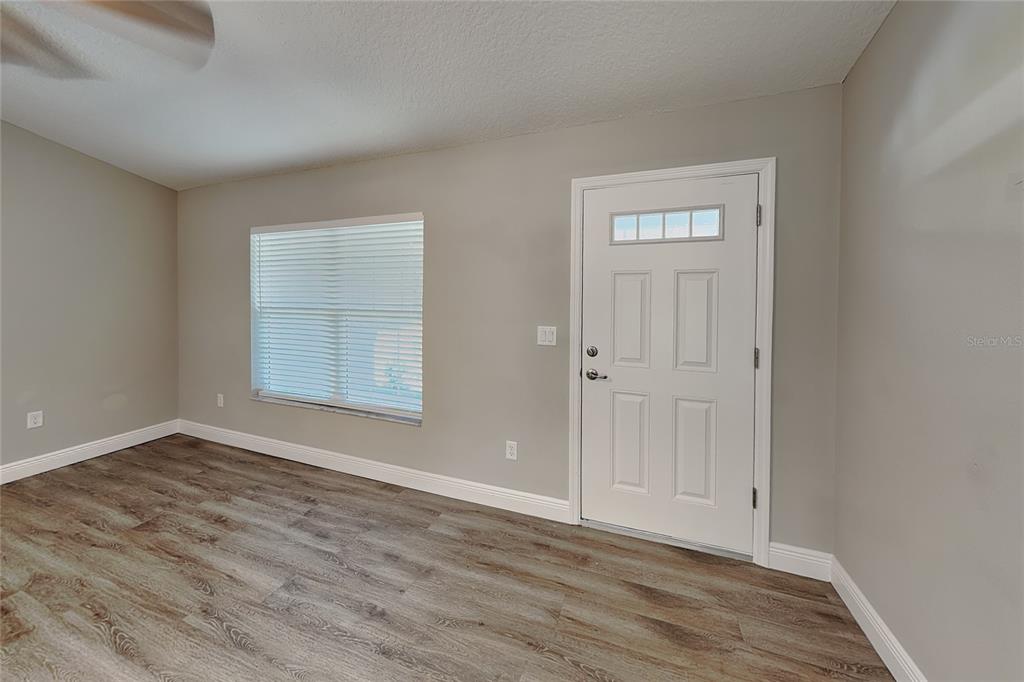 An empty room features light gray walls, wood-look flooring, a window with blinds, and a door — 7961 N PRIMROSE DRIVE, CITRUS SPRINGS, FL