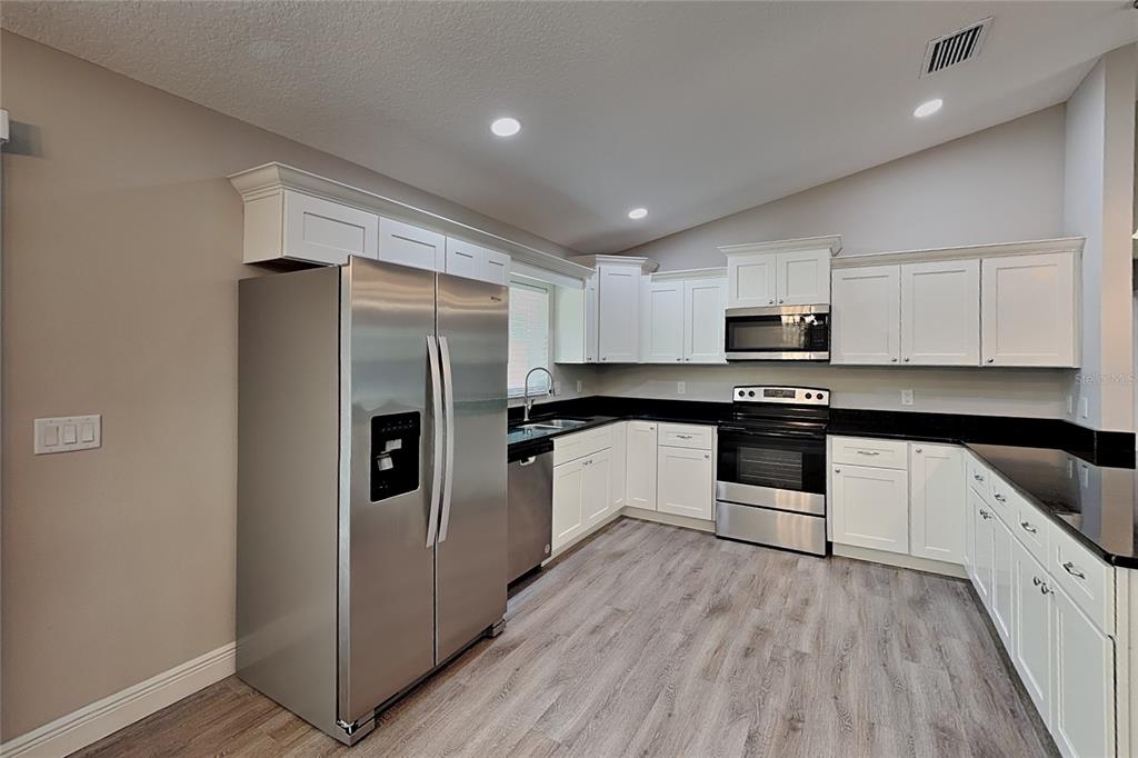 A kitchen features white cabinets, black countertops, stainless steel appliances, and light wood-look flooring — 7961 N PRIMROSE DRIVE, CITRUS SPRINGS, FL