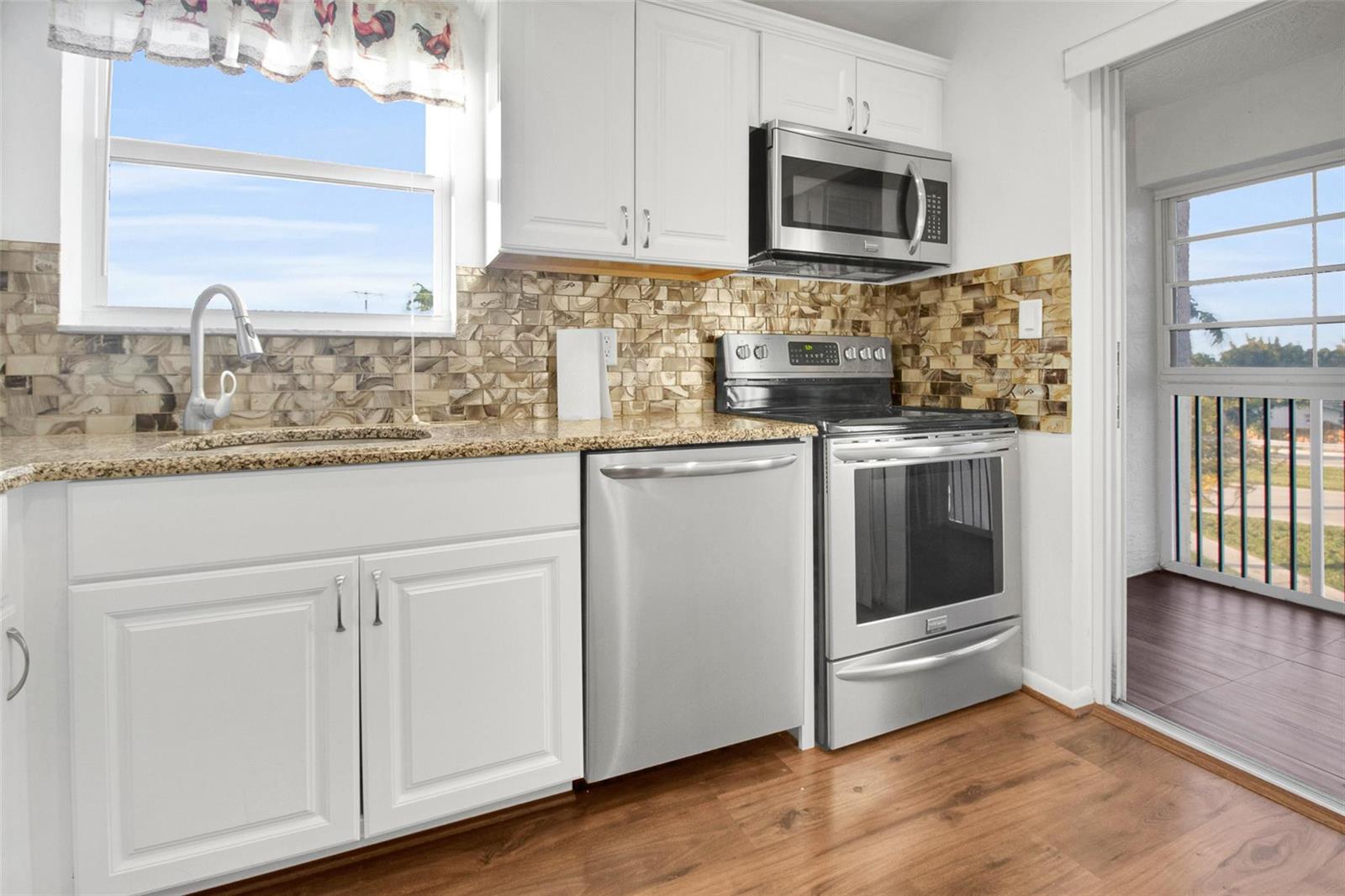 A kitchen features white cabinets, stainless steel appliances, granite countertops, and a mosaic tile backsplash — 6890 Royal Palm Boulevard # 312h, Margate FL 33063, MARGATE, FL