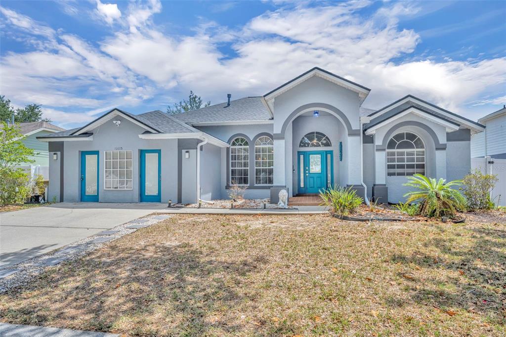 A single-story house with a light blue exterior, teal doors, and a concrete driveway — 15115 GREATER GROVES BOULEVARD, CLERMONT, FL
