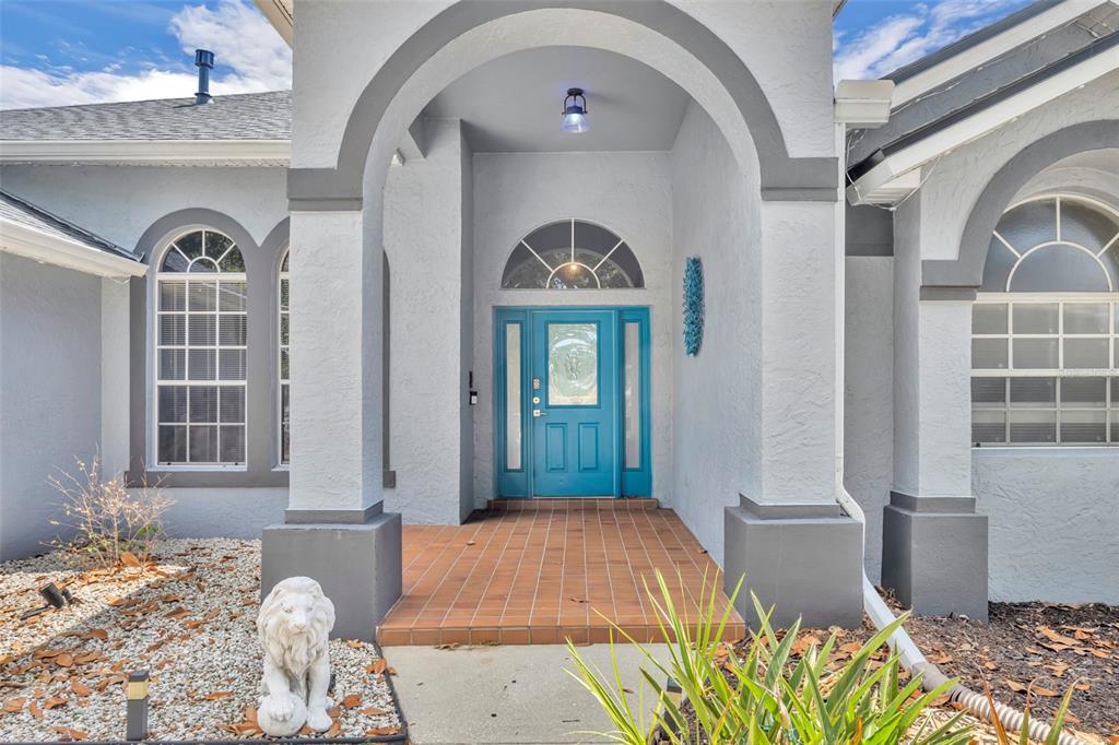 A bright blue front door is centered under a covered arched entryway with tiled flooring — 15115 GREATER GROVES BOULEVARD, CLERMONT, FL