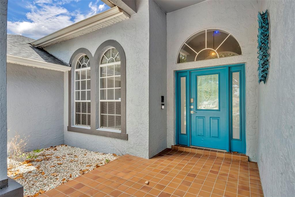 A bright blue front door with a transom window sits on a tiled porch — 15115 GREATER GROVES BOULEVARD, CLERMONT, FL