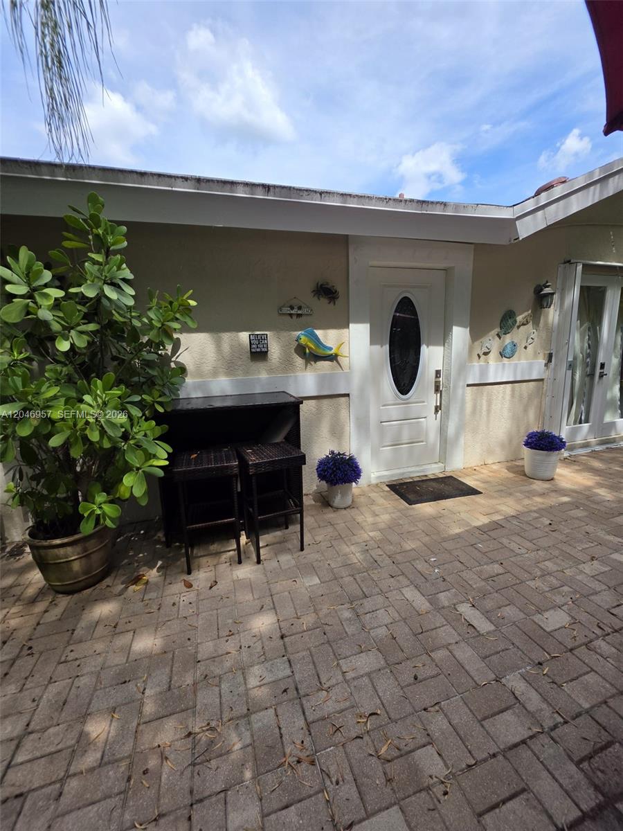 A paved patio area features a white front door, a potted plant, and outdoor furniture — 9760 SW 148th St, Miami FL 33176, MIAMI, FL