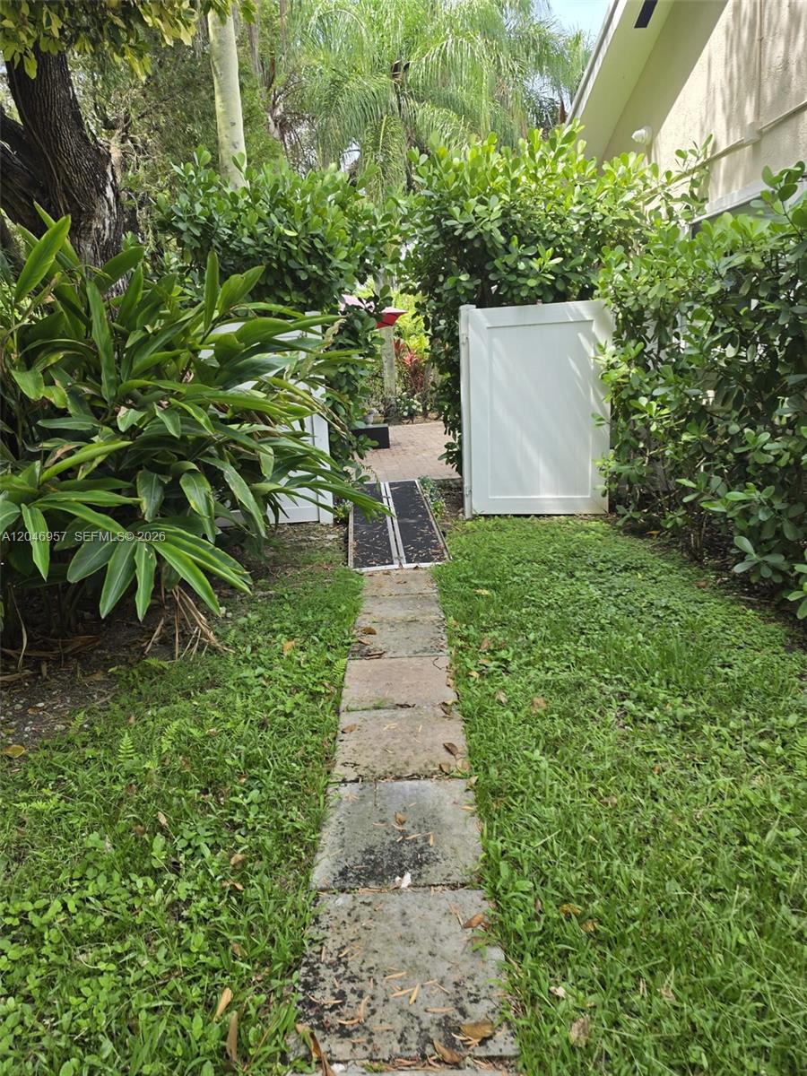 A stone path leads through a white gate toward a patio area with lush landscaping — 9760 SW 148th St, Miami FL 33176, MIAMI, FL