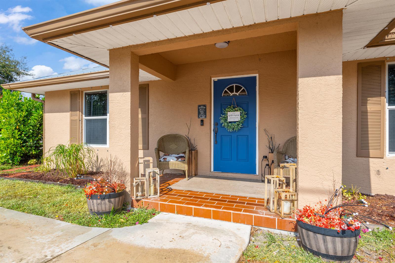 A blue front door with a wreath sits under a covered porch with tiled steps — 3789 SE 6th Street, Okeechobee FL 34974, OKEECHOBEE, FL