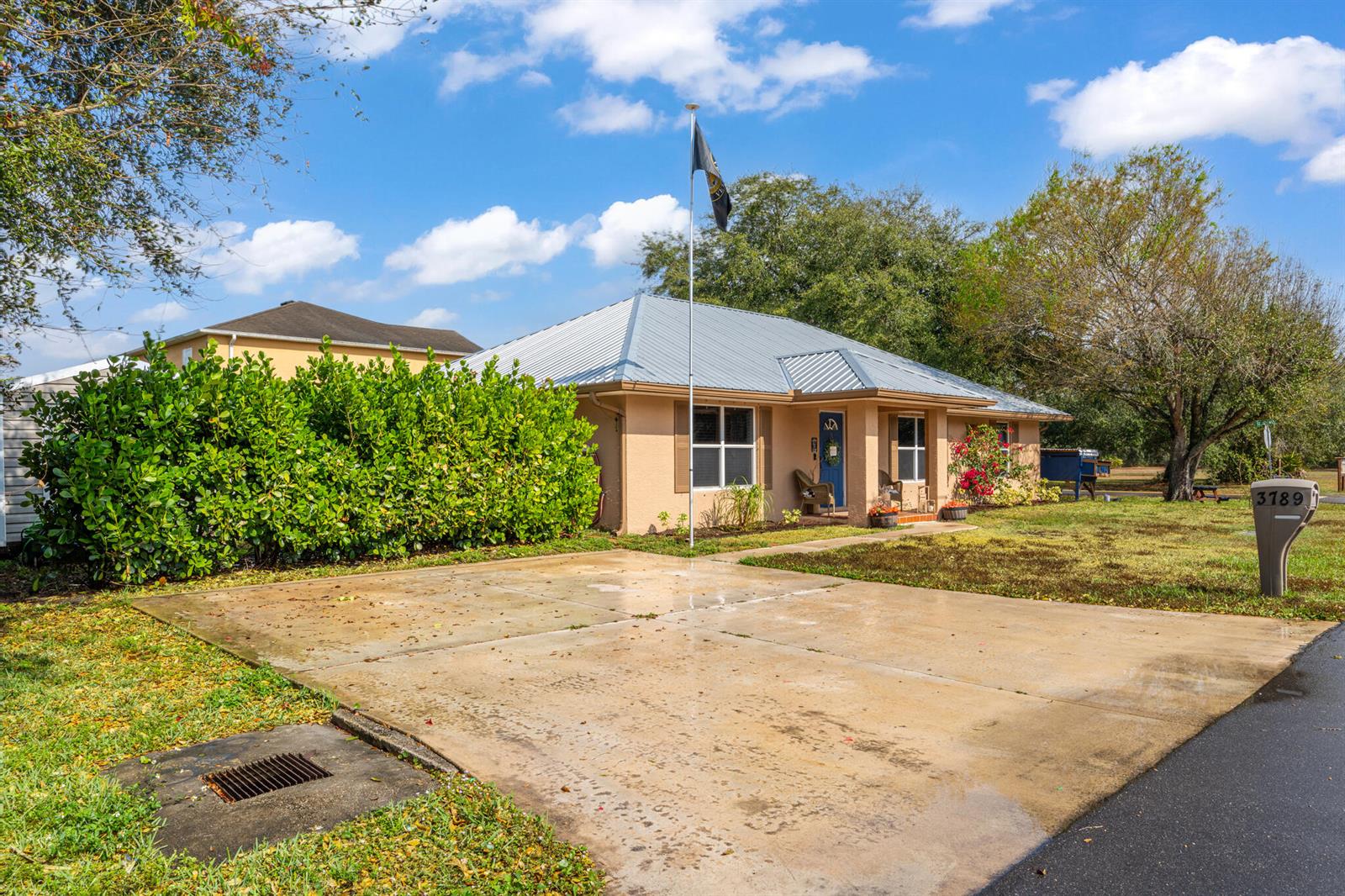 A single-story house with a metal roof, beige stucco exterior, and a concrete driveway — 3789 SE 6th Street, Okeechobee FL 34974, OKEECHOBEE, FL