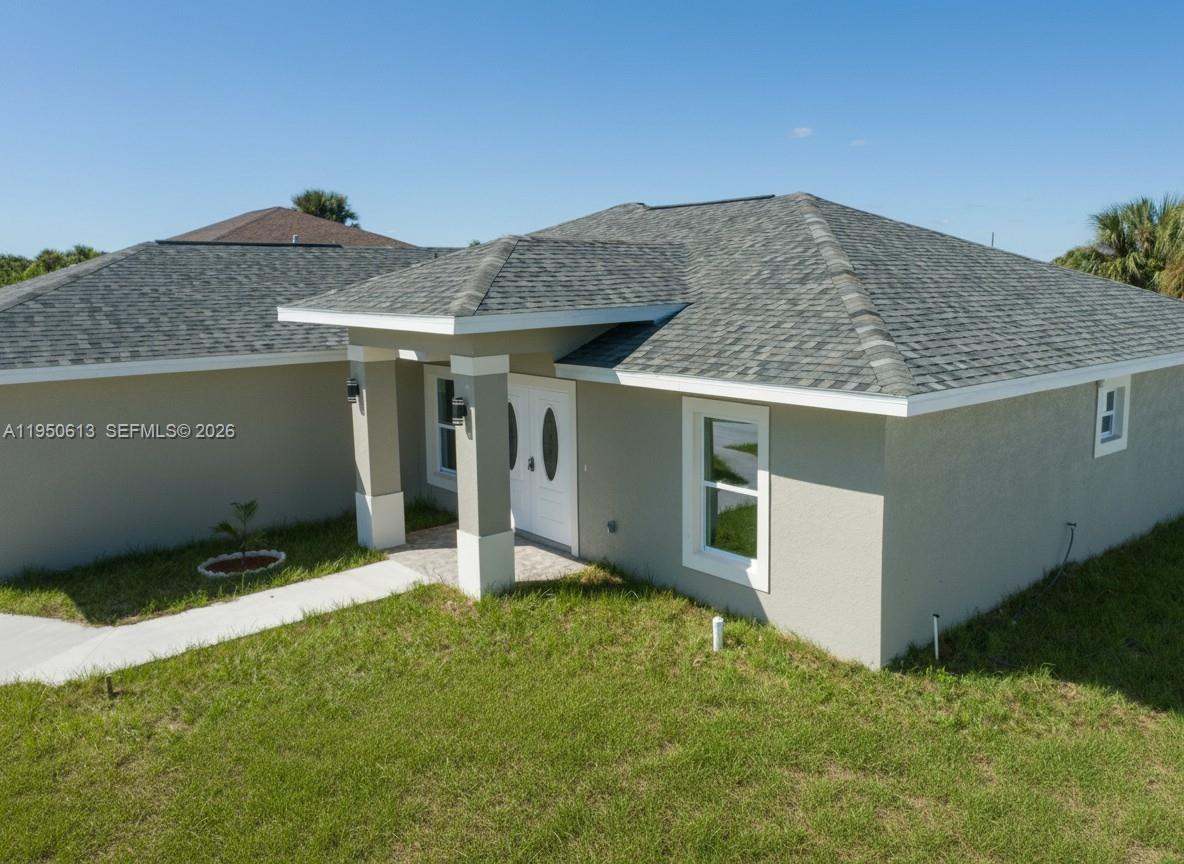An exterior view of a single-story house with a gray stucco facade and shingled roof — 8038 Sunrise Cir., La Belle FL 33935, LA BELLE, FL