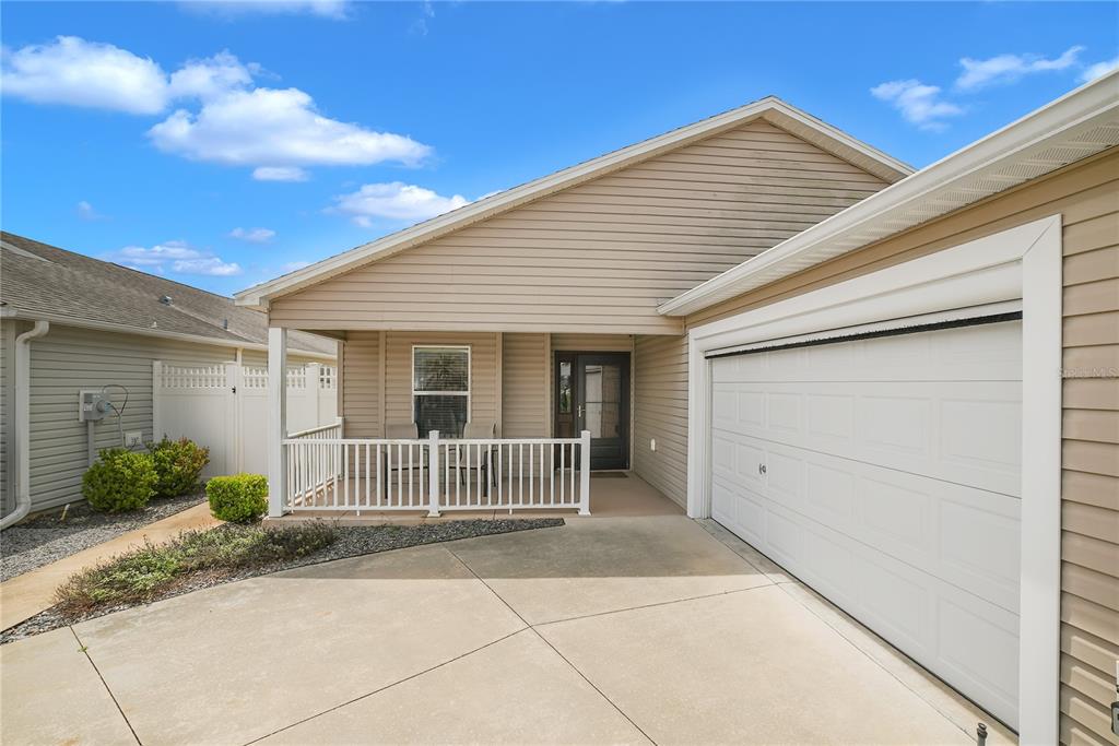 A beige house exterior features a front porch, a white garage door, and a driveway — 2604 ALCADE PLACE, THE VILLAGES, FL