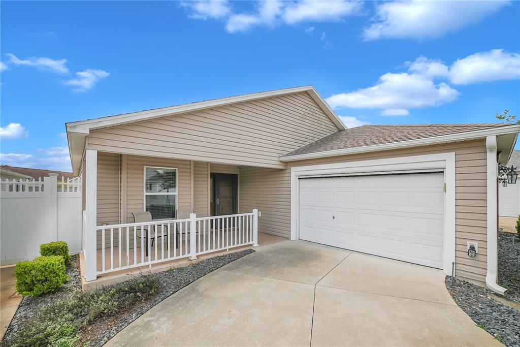 A single-story house features beige vinyl siding, a white front porch, and a one-car garage — 2604 ALCADE PLACE, THE VILLAGES, FL