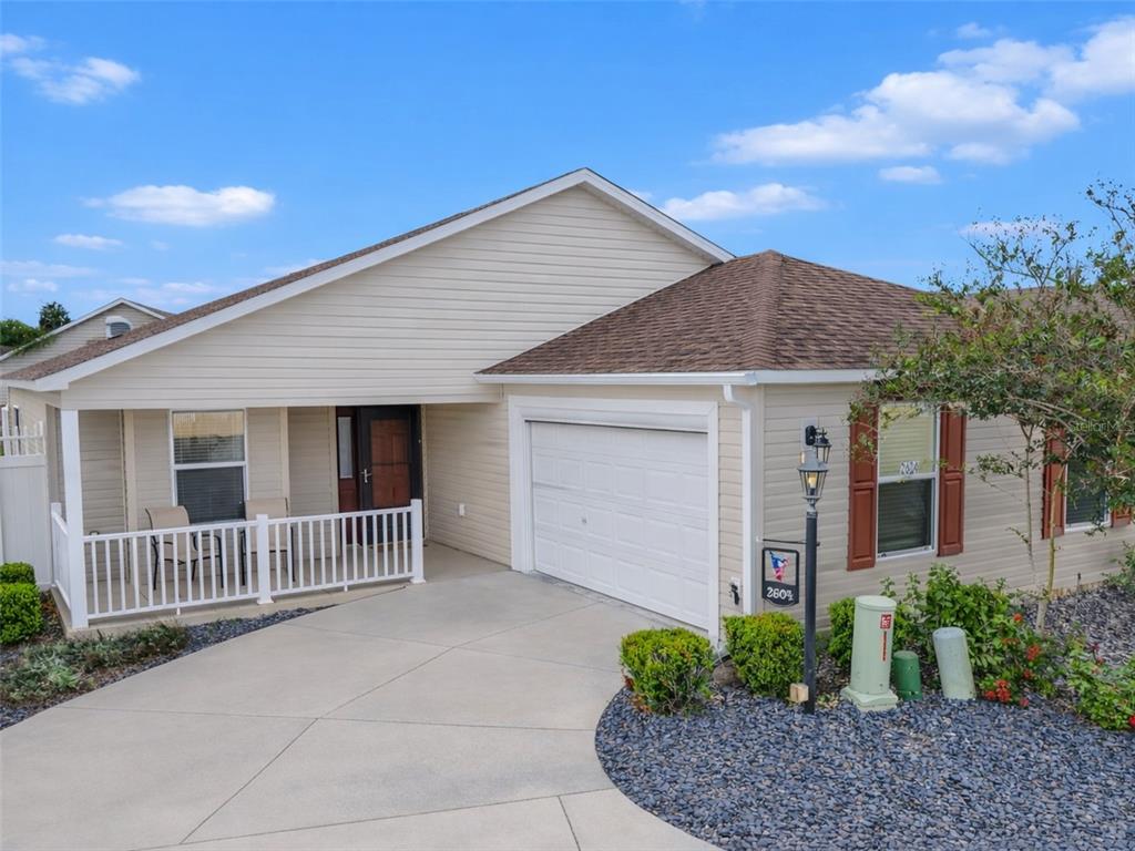 A single-story house with beige siding, a white garage door, and a front porch — 2604 ALCADE PLACE, THE VILLAGES, FL