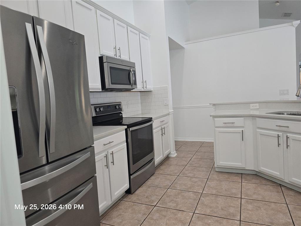 A kitchen features white cabinets, stainless steel appliances, and light-colored tile flooring — 14751 SEATTLE SLEW PLACE, ORLANDO, FL