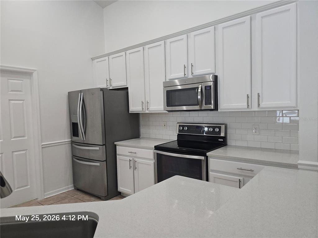 A kitchen features white cabinets, stainless steel appliances, a subway tile backsplash, and quartz countertops — 14751 SEATTLE SLEW PLACE, ORLANDO, FL