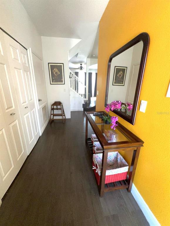 A hallway features dark wood flooring, a glass-topped console table, and a mirror on a yellow wall — 1209 S BEACH CIRCLE, KISSIMMEE, FL