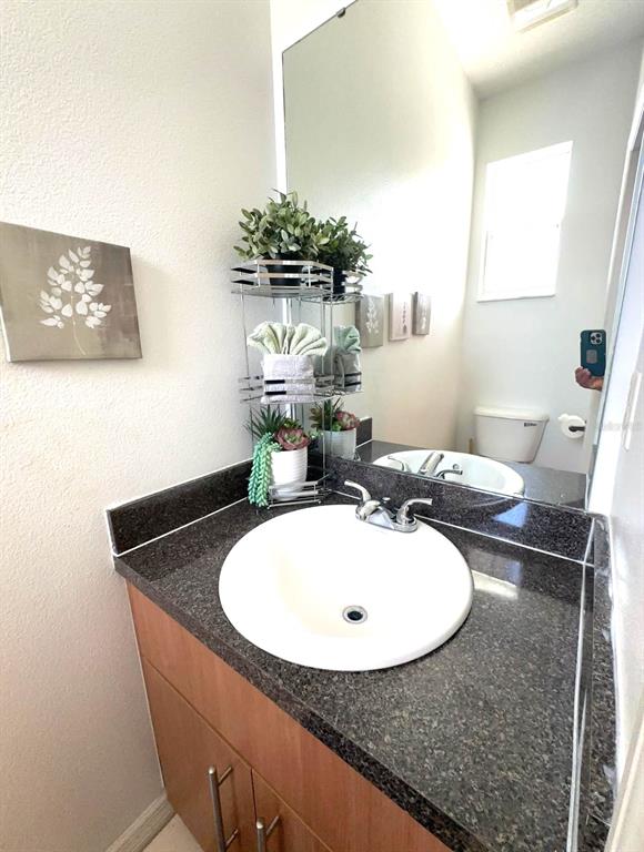 A bathroom features a white sink, dark granite countertop, wooden vanity, and a tiered shelf — 1209 S BEACH CIRCLE, KISSIMMEE, FL