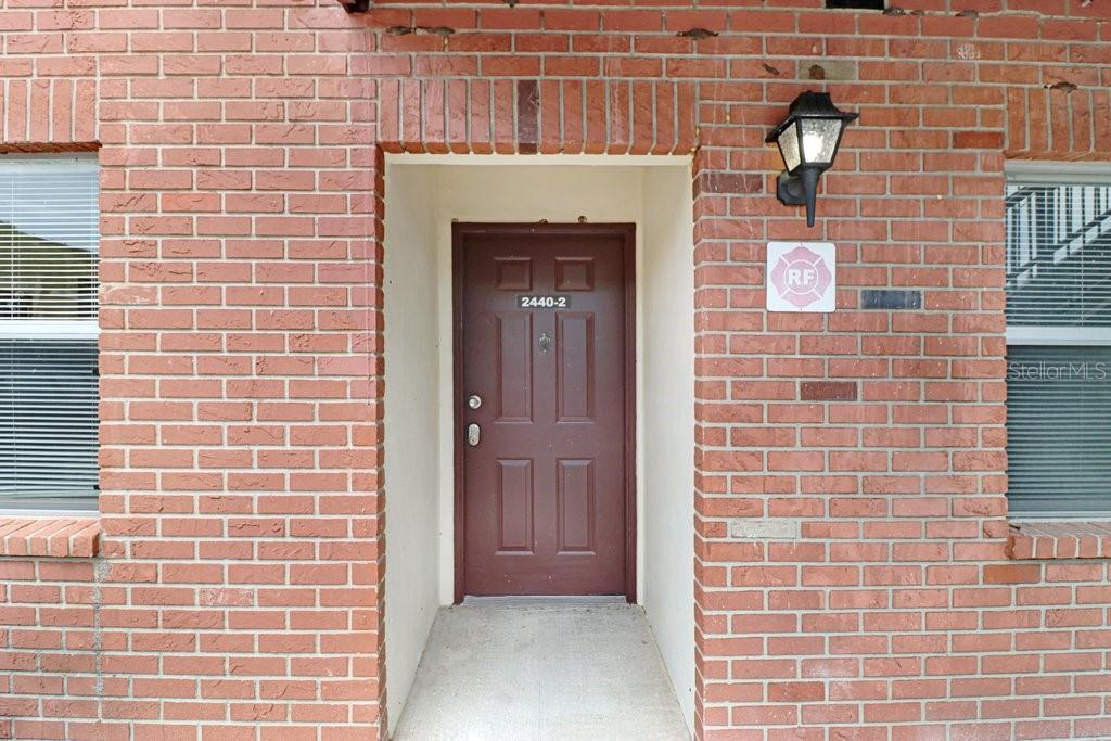 A brown front door is centered within a red brick exterior wall — 2440 ENTERPRISE ROAD UNIT 2, CLEARWATER, FL