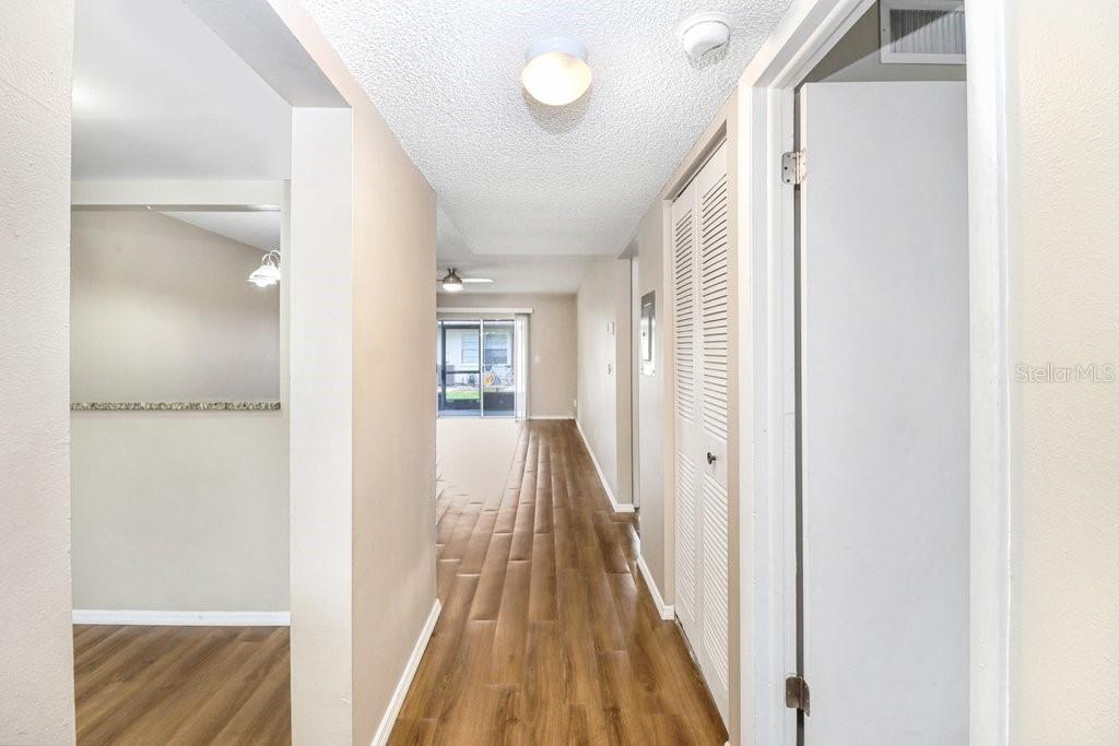 A hallway with wood-look flooring leads toward a living area with a sliding glass door — 2440 ENTERPRISE ROAD UNIT 2, CLEARWATER, FL