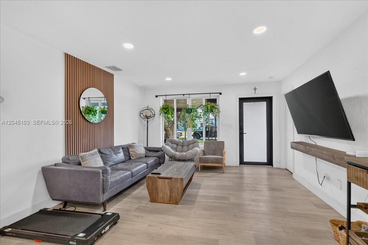 A living room features a grey sofa, wood-slat wall accent, and a wall-mounted television — 1131 N 75th Ave, Hollywood FL 33024, HOLLYWOOD, FL