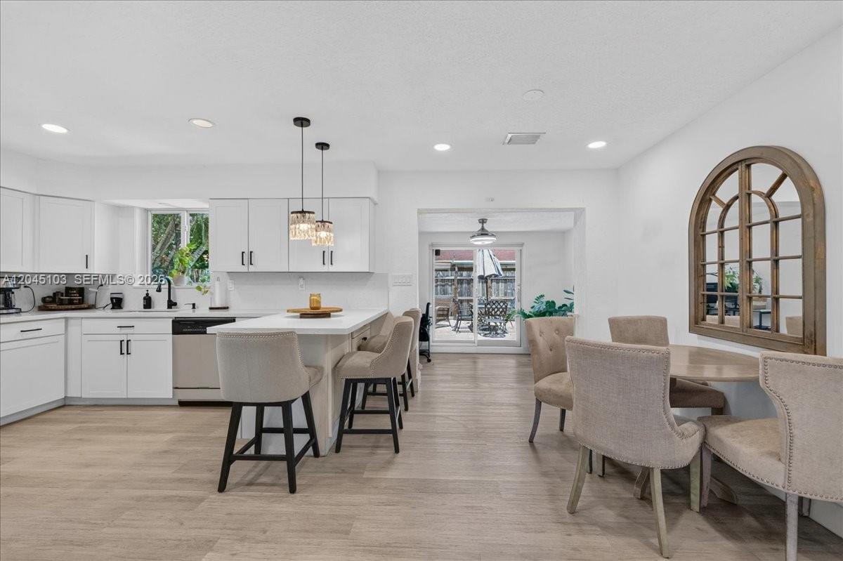 A bright kitchen features white cabinetry, a central island with bar seating, and an adjacent dining area — 1131 N 75th Ave, Hollywood FL 33024, HOLLYWOOD, FL