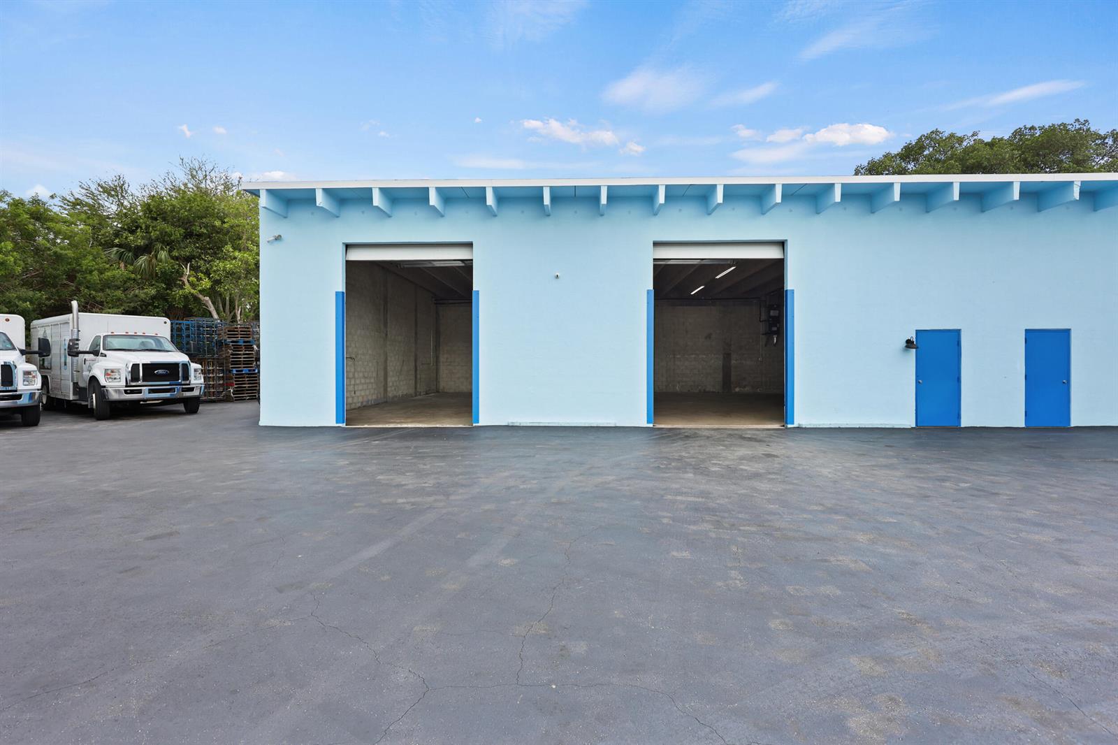 A light blue industrial building features two open garage bays and two blue entry doors — 2605 Kelly Lane, FL 33460, FL