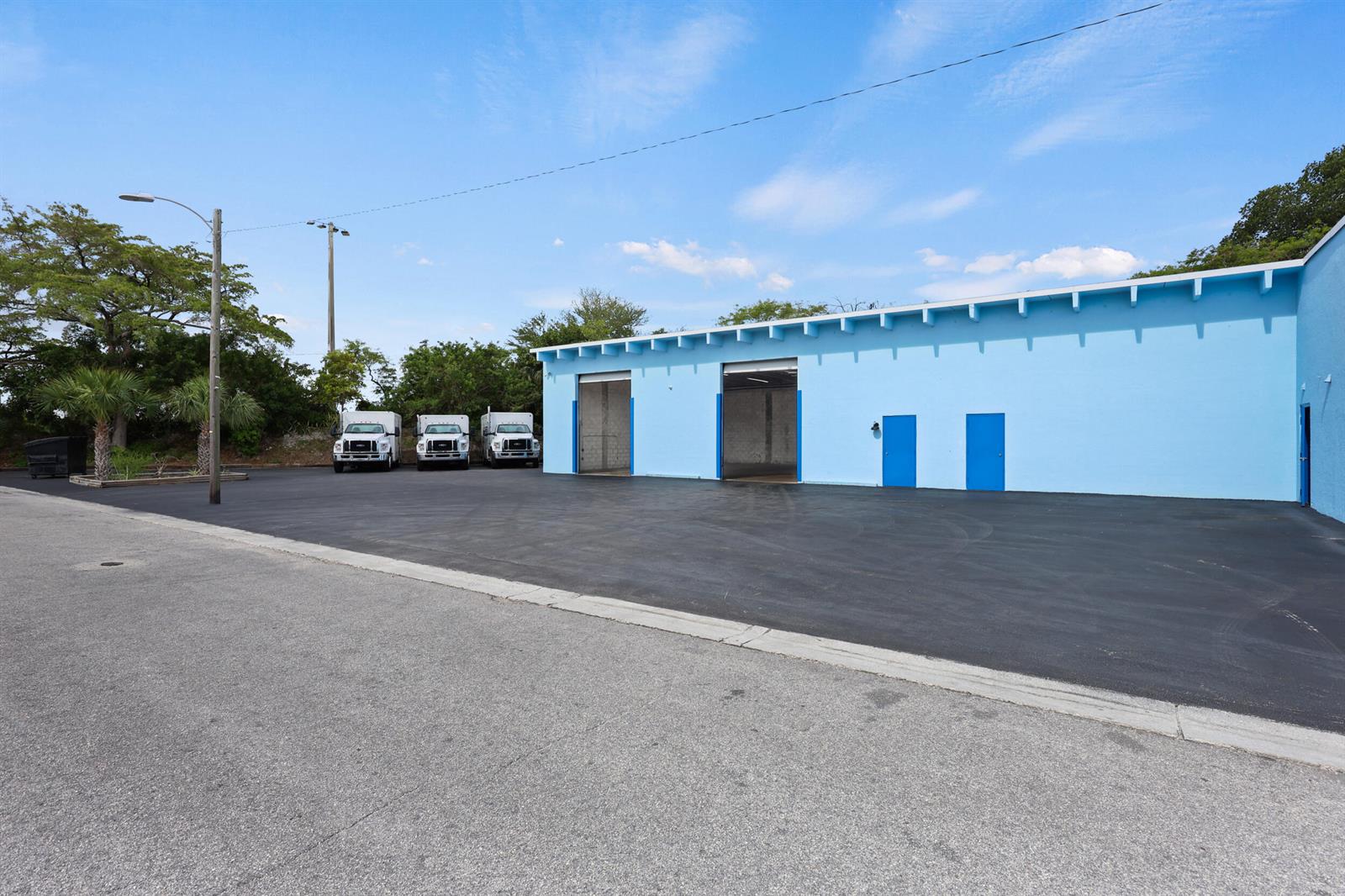 A light blue industrial warehouse building features two open bay doors and three white trucks — 2605 Kelly Lane, FL 33460, FL