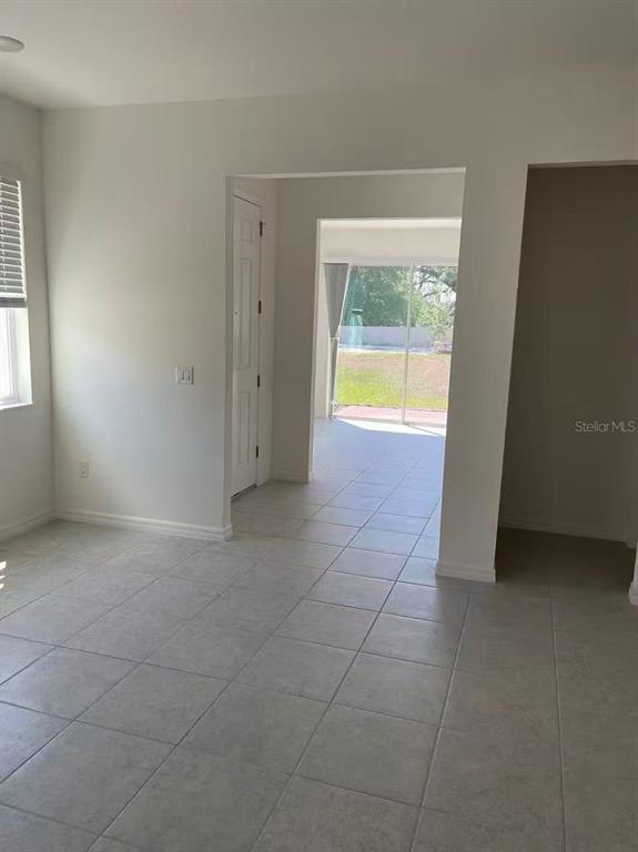 A room with light-colored tile flooring leads to a doorway with a view of grass — 34224 ROGALLO LANE, WESLEY CHAPEL, FL