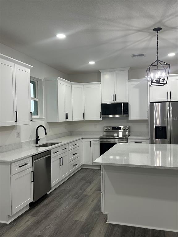 A modern kitchen features white cabinets, stainless steel appliances, a large island, and wood-look flooring — 13311 MIDWAY AVENUE, ASTATULA, FL