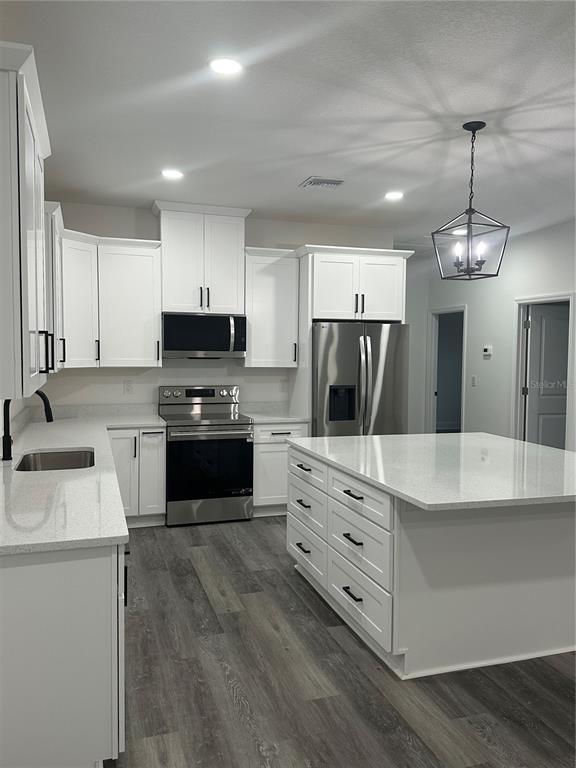 A modern kitchen features white cabinets, stainless steel appliances, a large island, and wood flooring — 13311 MIDWAY AVENUE, ASTATULA, FL