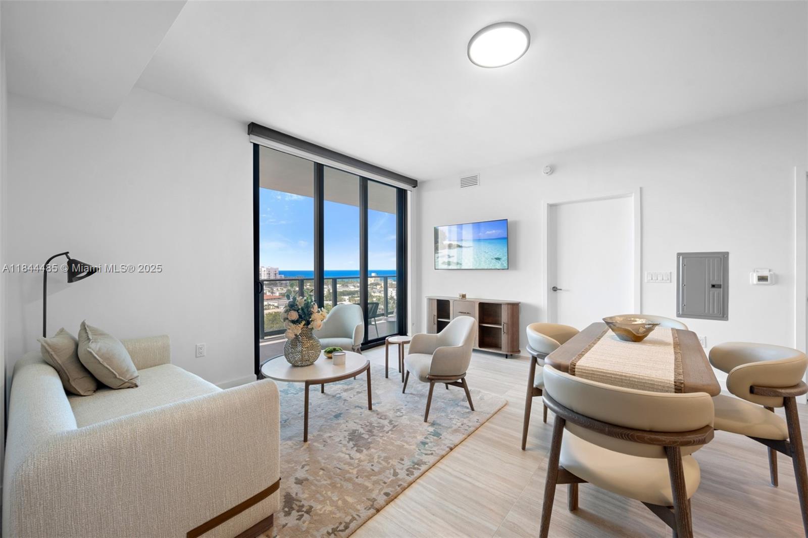 A bright living and dining area features light wood floors, modern furniture, and ocean views — 580 72nd St # 1009, Miami Beach FL 33141, MIAMI BEACH, FL