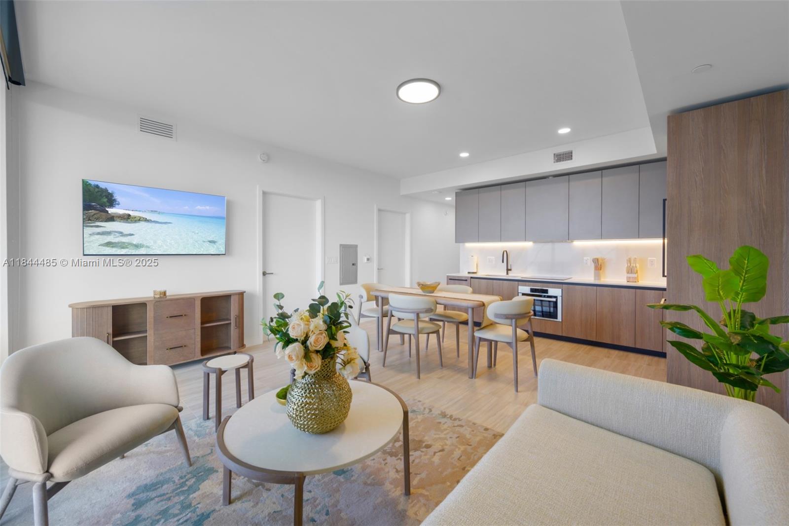 A modern open-concept living room and kitchen featuring light wood flooring and neutral furniture — 580 72nd St # 1009, Miami Beach FL 33141, MIAMI BEACH, FL