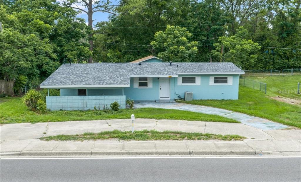 A light blue single-story house with a gray shingled roof sits behind a concrete driveway — 1214 SE 36TH AVENUE, OCALA, FL