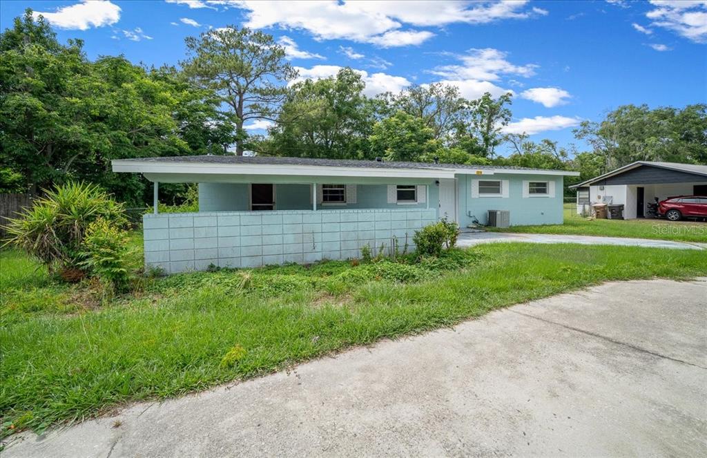 A light blue single-story house features a concrete block wall and a covered porch area — 1214 SE 36TH AVENUE, OCALA, FL