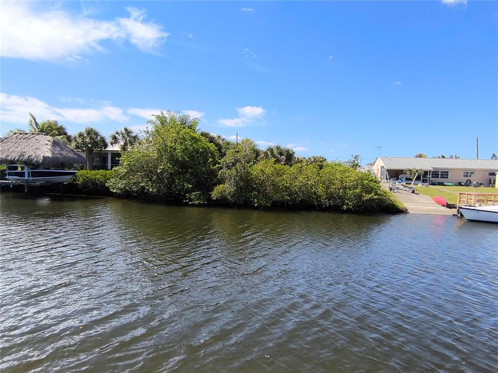 A canal view shows a boat lift, dense shoreline vegetation, and a house with a ramp — 19170 NEW HAVEN COURT, PORT CHARLOTTE, FL