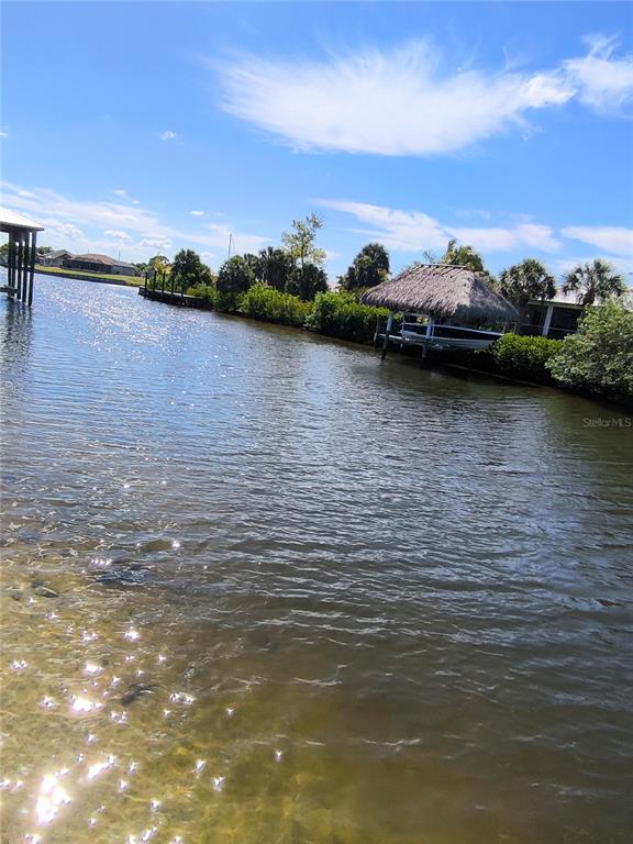A canal view features a thatched-roof boat lift and lush vegetation along the shoreline — 19170 NEW HAVEN COURT, PORT CHARLOTTE, FL