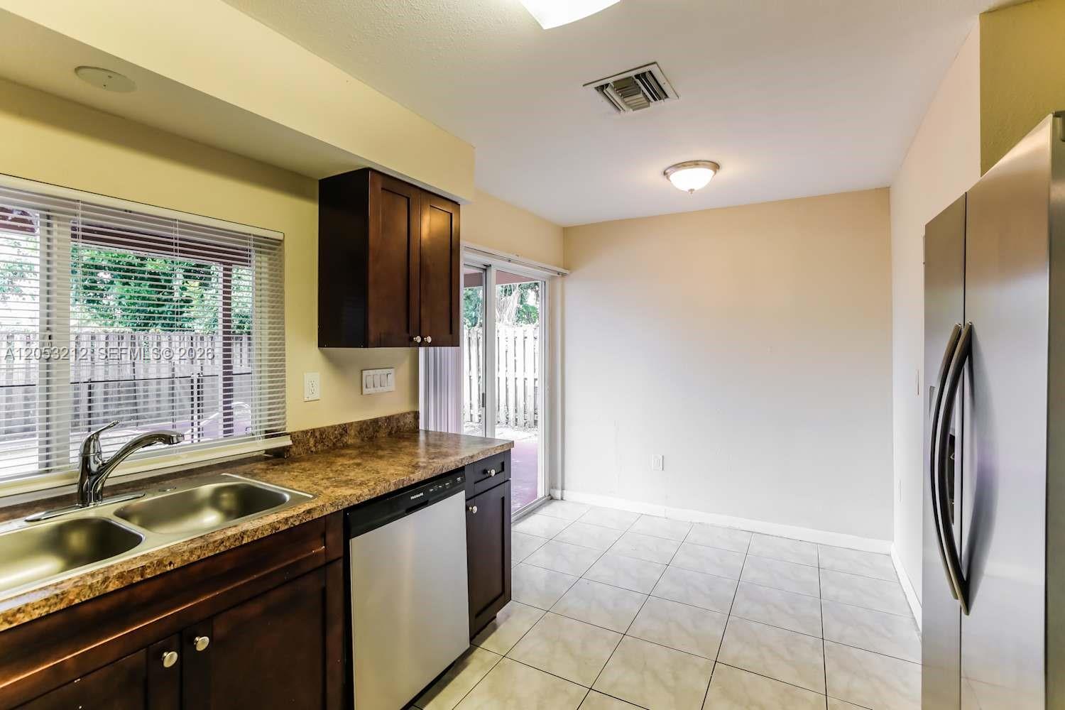 A kitchen features dark wood cabinets, laminate countertops, stainless steel appliances, and tile flooring — SUNRISE, FL