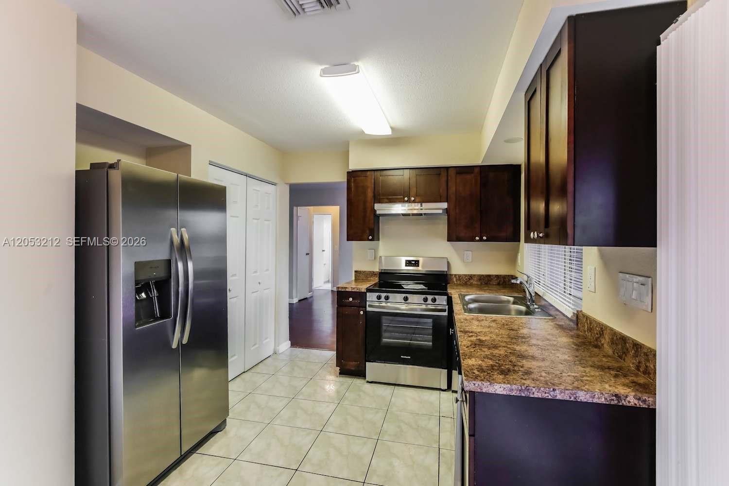A kitchen features dark wood cabinets, stainless steel appliances, and brown laminate countertops — SUNRISE, FL