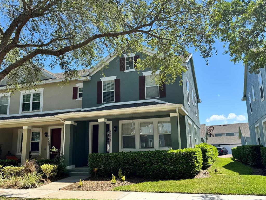 A two-story green townhouse features a front porch, dark shutters, and a manicured hedge — 8484 LEELAND ARCHER BOULEVARD, ORLANDO, FL