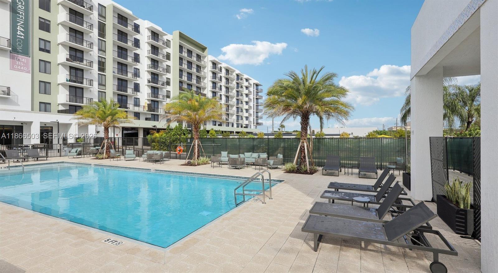 An outdoor swimming pool area features lounge chairs, palm trees, and a large apartment building — 4465 Griffin Road # B5, Davie FL 33314, DAVIE, FL