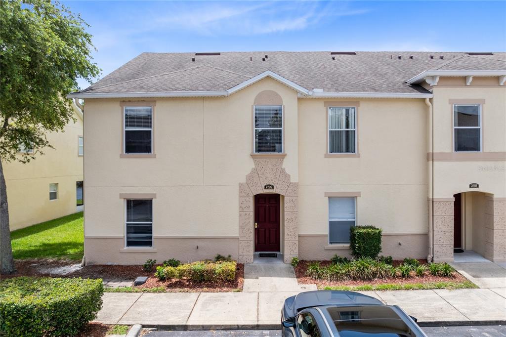 A two-story townhouse exterior features beige stucco walls, a dark red front door, and shingles — 2799 CLUB CORTILE CIRCLE UNIT 2799, KISSIMMEE, FL