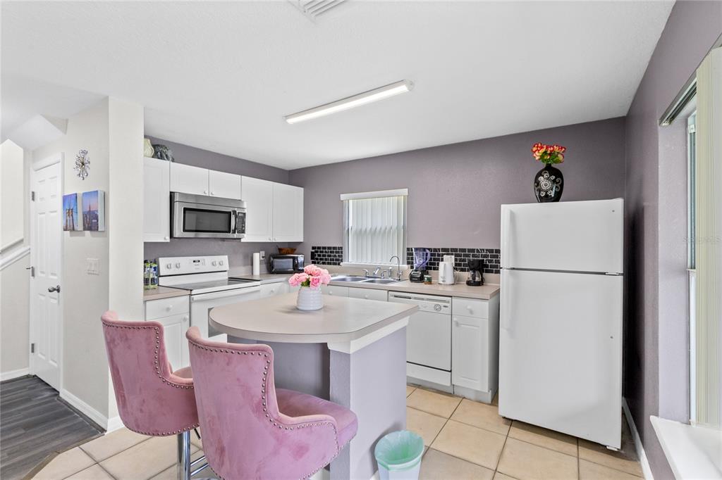 A kitchen features white cabinetry, stainless steel appliances, a central island, and pink bar stools — 2799 CLUB CORTILE CIRCLE UNIT 2799, KISSIMMEE, FL
