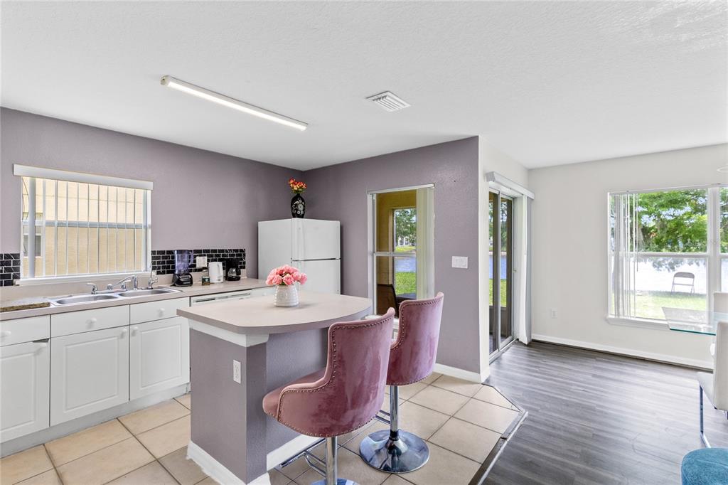 A kitchen with white cabinets, a small island with pink stools, and a sliding door — 2799 CLUB CORTILE CIRCLE UNIT 2799, KISSIMMEE, FL