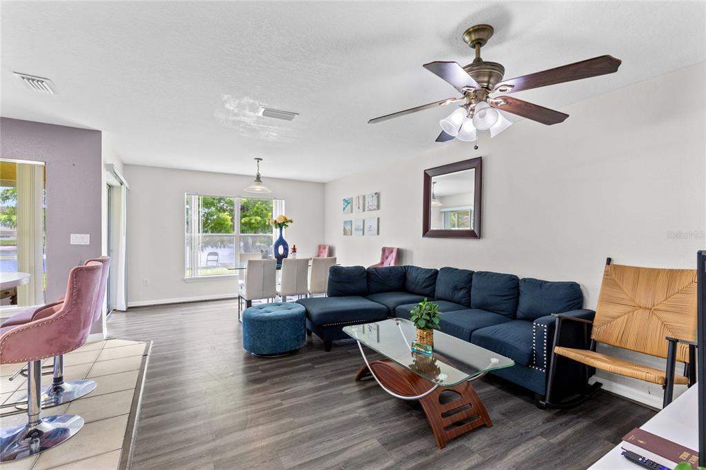 A living room with a blue sectional sofa, glass coffee table, and adjacent dining area — 2799 CLUB CORTILE CIRCLE UNIT 2799, KISSIMMEE, FL
